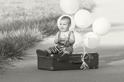 little traveler sits on the roadside in an old suitcase.Black and white toned photo in vintage style