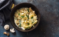 Italian pasta( fettuccini) with mushrooms, chicken meat, spinach and cream sauce in a skillet on a grunge dark background. Flat lay. Copy space