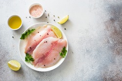 Raw tilapia fillet with lime and spices on a gray stone background. Flat lay. Copy space