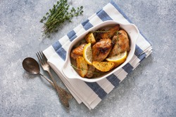 Chicken drumsticks baked with potatoes , lemon and herbs in white ceramic pan. Top view