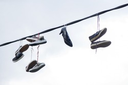 Old sneakers and high heel shoes hanging on electrical wire on overcast background