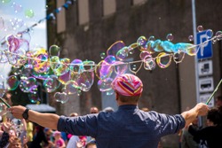 A freelance clown blowing hundreds of tiny, small and big bubbles at outdoor festival in city center. Concept of entertainment, birthdays. Kids having fun. Shower of bubbles flying in the happy crowd
