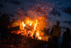Large burning bonfire with soft glowing flame and sparkles flying all around. Romantic summer evening, people relaxing and enjoying calmness at the seaside during the Night of ancient lights. 