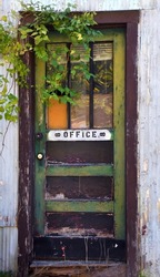 Abandoned building once housed the office for this derelict business in a ghost town called Pepper Sauce Alley, in Calico Rock, Arkansas.  Door is faded green and brown with broken glass.