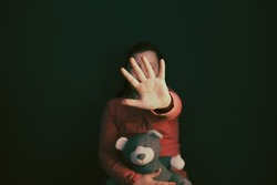 Child violence and abused concept. Little girl sitting in a dark room, showing stop sign