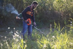 man trimming weed with weed trimmer in summer