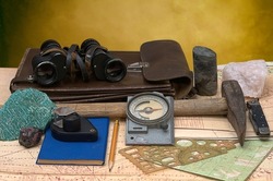 Geological fieldwork tools: map case, geological hammer, compass, magnifying glass, pocket knife, binoculars, drill core, rock samples, topographic and geological maps