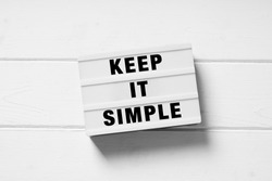 keep it simple text on lightbox sign, minimal flat lay design on white wooden background, simplicity or minimalism concept