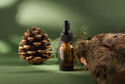 Cosmetic bottle with dropper on a wooden bark and moss. Pine tree essential oils on a dark green background.