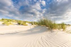 Sand dunes with grass under a blue sky with clouds