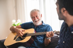 Eldery Father and adult son are playing music and sing a song together. The happy family concept with the guitar instrument.