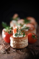 Delicate filo pastry Vol Au Vent canapes with fresh tiger prawns, soft cheese, chives, tomatoes, cucumber and dill garnish shot with creative lighting and generous accommodation for copy space.