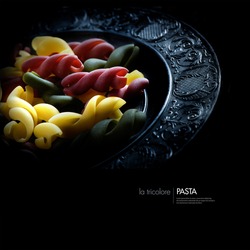 Creatively lit Italian tricolore pasta on a pewter plate against black. Concept image for vegetarian food. Copy space.