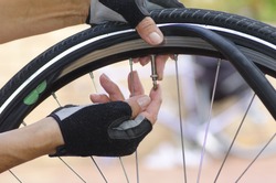 Close up image of a bicycle repair, with two hands in biker gloves, with valve, tube, alloys and a bike in the blurred background.