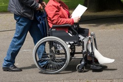 A man pushing a woman in a wheelchair with a injured leg