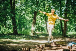 Balancing exercise outdoors. Mature woman standing on one leg, exercising balance 