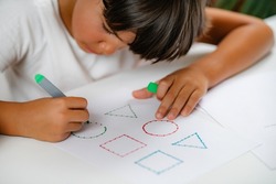 Preschooler boy sitting at the desk, drawing shapes 