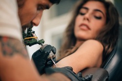 Tattoo artist creating a tattoo on a girl's arm. Focus on tattoo machine