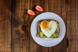Toast with avocado and egg in heart shape and strawberries