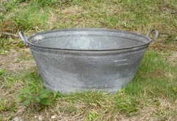 Empty tin bath standing on rough grass and weeds