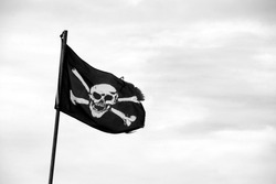 Ragged pirate flag with skull and crossbones flying from flagpole - monochrome processing