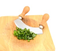 Chopped fresh basil leaves with a rocking knife on a wooden chopping board, isolated on a white background
