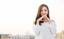 Portrait of young beautiful asian woman hands gesture in heart shape on city sky roof top. Smile face asian lady girl wear casual cloth. Japanese girl lifestyle, lovely woman valentines’ day concept 