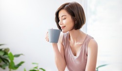 Portrait of young beautiful asian woman hands holding coffee cup morning spring time in white bedroom. Happy cheerful relaxing in summer. Korean asian makeup wakeup university asia lifestyle concept
