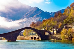 Tuscany. Borgo a Mozzano. The Serchio River. The cold water of the river reflects the ancient asymmetrical arches of the Devil's Bridge. Sunny windy December morning. Italy