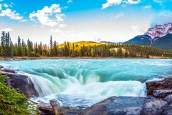 Travel to Jasper Park, Canada. The waters of a melting mountain glacier feed the booming waterfall of Athabasca. Clear autumn evening at sunset. The concept of extreme and ecological tourism