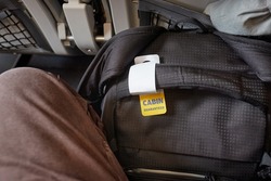 Cabin bag on a flight with tag for carry-on size guarantee fit between legs and under seat in front