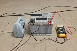 Charging a car starter battery, in a garage, monitoring state with digital multimeter