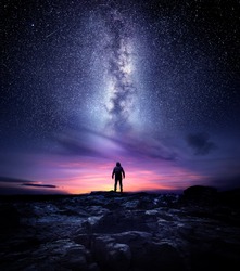 Night time long exposure landscape photography. A man standing in a high place looking up in wonder to the Milky Way galaxy, photo composite.