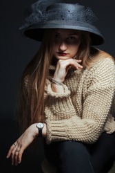 Studio portrait of a girl in a knitted sweater with a dark hat hiding her face. Shot in dark colors. The concept of isolation