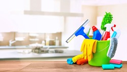 Cleaning items in a bucket on a wooden table infront of a kitchen background. Cleaning service concept with copy space