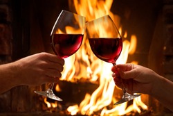 Hands toasting wine glasses in front of lit fireplace
