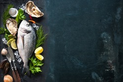 Delicious fresh fish and oysters with aromatic herbs, spices and vegetables on dark slate plate