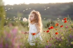 Portrait of a cute little girl in sunny summer day at green nature background. Summer joy - lovely girl blowing dandelion. 