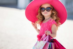 cute little girl in fashionable hat on shopping. portrait of a kid with shopping bags. child in dress, sunglasses and shoes near shopping mall having fun. shopping. girl. fashion