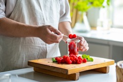 Man taking raspberries from jar at kitchen.
