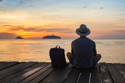 wanderlust travel, tourist with backpack sitting near the sea, man enjoying sunset, solo traveler backpacker in Asia