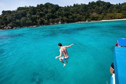 young man jumping to the sea from yacht near the beach of paradise island