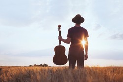 music festival background, silhouette of musician artist with acoustic guitar at sunset field
