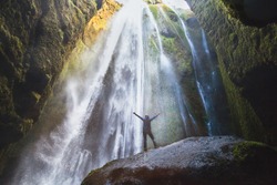 travel to Iceland, person with raised hands standing in waterfall Gljufrabui, inspired happy traveler enjoying nature, adventure concept