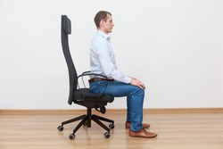 caucasian man sitting on the edge of office chair in correct posture