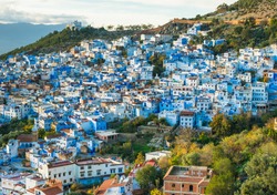Chefchaoeun blue city in Morocco panoramic view on sunset with blue houses and green hills around with soft focus