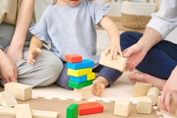 Asian little girl playing with building blocks with her parents, no face
