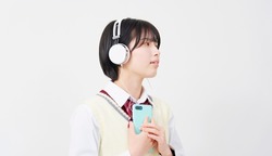 Asian high school student listening to music with a smart phone in white background