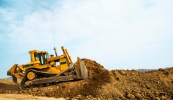 Bulldozer at a construction site shovels mountain soil into a heap
