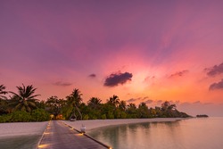 Sunset on Maldives island, luxury resort hotel and wooden pier jetty. Wonderful colorful sky clouds and beach sea horizon. Summer romantic vacation holiday, travel concept. Paradise sunset landscape